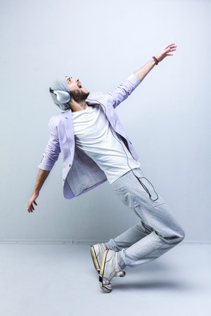 man in pink jacket, grey pants, cap, old sneakers and headphones dancing against grey backgroundの写真素材
