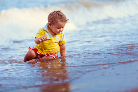Boy in yellow shirt, red shorts, sit on the beach close to the water, playの写真素材