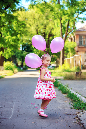 Cute little girl with pink balllons outdoors in the courtyardの写真素材