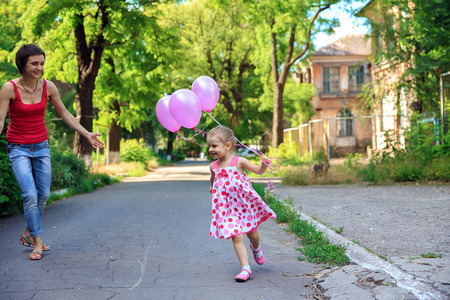 Amazing emitions playing mother and daughter in the air baloons in the courtyard. Beautiful girl.の写真素材