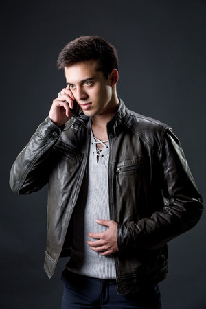 dark-haired guy in a leather jacket speaking by the mobile phoneの写真素材