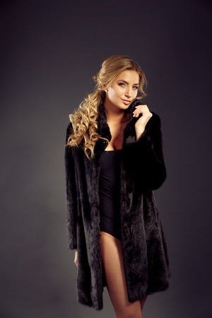 Fashion seductive blond hair lady in an elegant fur coat and black underwear on a dark backgroundの写真素材