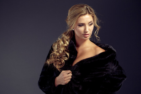 Fashion seductive blond hair lady in an elegant fur coat and black underwear on a dark backgroundの写真素材