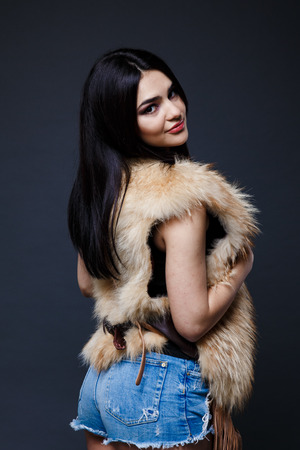 Fashion seductive dark hair lady in an elegant fur coat on a dark backgroundの写真素材