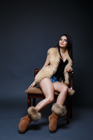 Fashion seductive dark hair lady in an elegant fur coat on a dark backgroundの写真素材