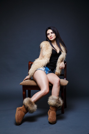 Fashion seductive dark hair lady in an elegant fur coat on a dark backgroundの写真素材