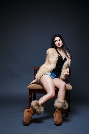 Fashion seductive dark hair lady in an elegant fur coat on a dark backgroundの写真素材
