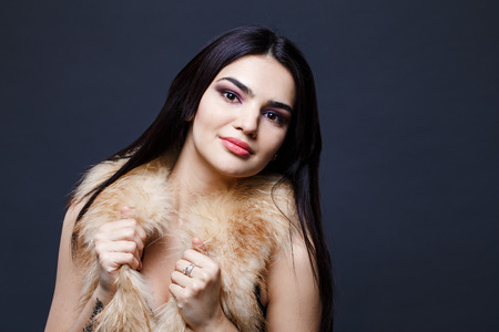 Fashion seductive dark hair lady in an elegant fur coat on a dark backgroundの写真素材