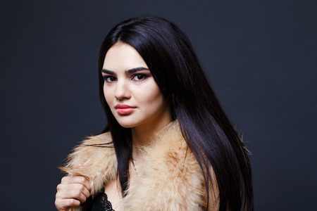 Fashion seductive dark hair lady in an elegant fur coat on a dark backgroundの写真素材