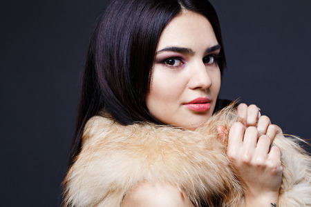 Fashion seductive dark hair lady in an elegant fur coat on a dark backgroundの写真素材
