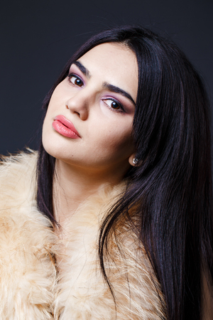 Fashion seductive dark hair lady in an elegant fur coat on a dark backgroundの写真素材