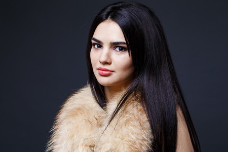 Fashion seductive dark hair lady in an elegant fur coat a on a dark backgroundの写真素材