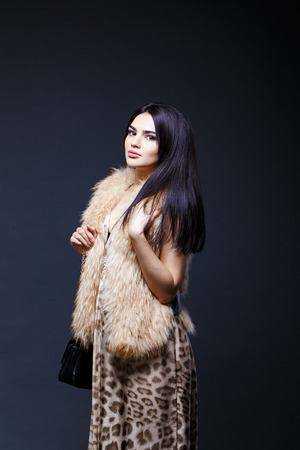 Fashion seductive black hair lady in an elegant fur coat and leopard dress on a dark backgroundの写真素材