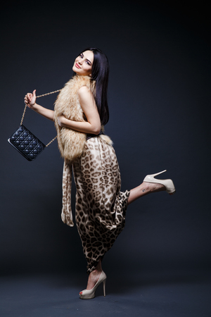 Fashion seductive black hair lady in an elegant fur coat and leopard dress on a dark backgroundの写真素材