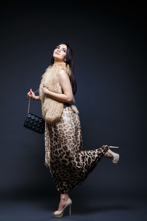 Fashion seductive black hair lady in an elegant fur coat and leopard dress on a dark backgroundの写真素材