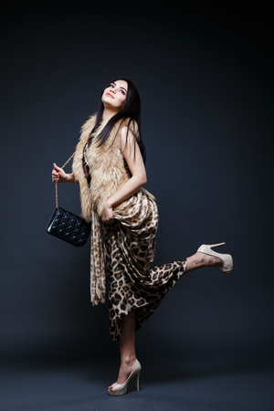 Fashion seductive black hair lady in an elegant fur coat and leopard dress on a dark backgroundの写真素材