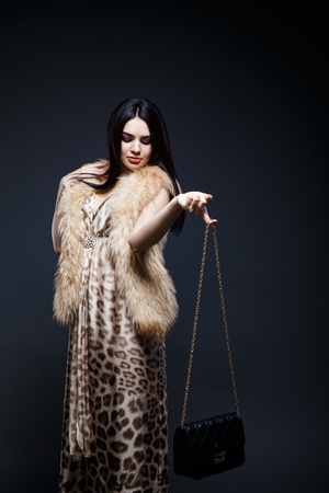Fashion seductive black hair lady in an elegant fur coat and leopard dress on a dark backgroundの写真素材