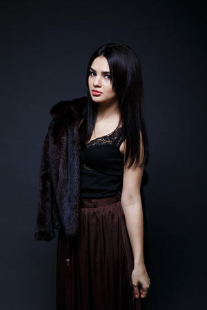 Fashion seductive black hair lady in an elegant fur coat and black underwear, brown skirt on a dark backgroundの写真素材