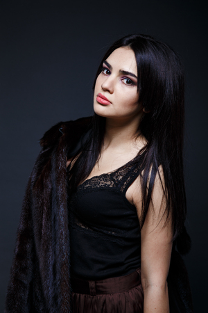 Fashion seductive black hair lady in an elegant fur coat and black underwear, brown skirt on a dark backgroundの写真素材