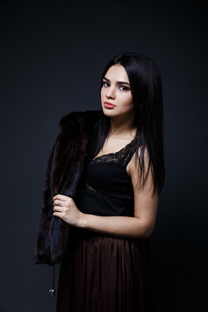 Fashion seductive black hair lady in an elegant fur coat and black underwear, brown skirt on a dark backgroundの写真素材