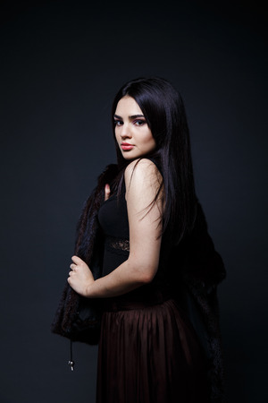 Fashion seductive black hair lady in an elegant fur coat and black underwear, brown skirt on a dark backgroundの写真素材