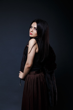 Fashion seductive black hair lady in an elegant fur coat and black underwear, brown skirt on a dark backgroundの写真素材