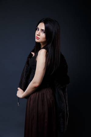 Fashion seductive black hair lady in an elegant fur coat and black underwear, brown skirt on a dark backgroundの写真素材