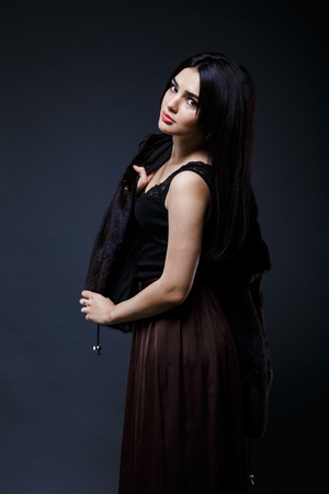 Fashion seductive black hair lady in an elegant fur coat and black underwear, brown skirt on a dark backgroundの写真素材