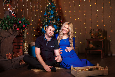 Pregnant woman and her husband in the living room, behind the decorated Christmas tree, the light give a cozy atmosphere.の写真素材