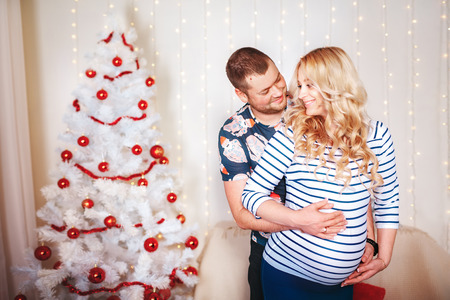 Pregnant woman and her husband in the living room, behind the decorated Christmas treeの写真素材