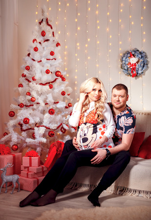 Pregnant woman and her husband in the living room, behind the decorated Christmas treeの写真素材