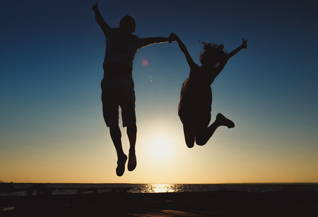 Silhouette Young couple in a jump on the sea beach at sunset.の写真素材