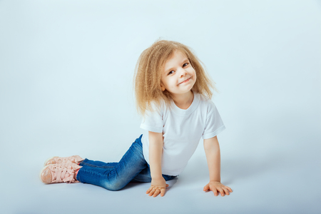 little girl 4 years old with curly hair wearing white shirt, blue jeans, pink boots sitting on the floor, smiling and looking at camera.の写真素材