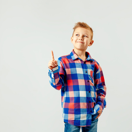 Boy wearing colorful plaid shirt, blue jeans, pointing up isolated. copyspase. Smile.の写真素材