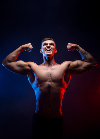 Handsome power athletic man bodybuilder. Fitness muscular body on dark smoke background. Perfect male. Awesome bodybuilder, tattoo, posing hands up. Viktory.の写真素材