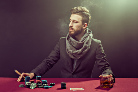 Elegant bearded player at pocker table with whisky and cigarの写真素材