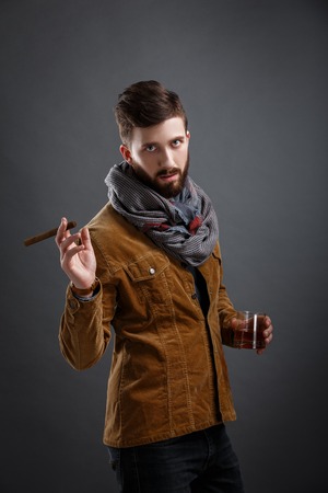 studio shot of bearded man with cigar and glass of whisky posing against of grey backgroundの写真素材