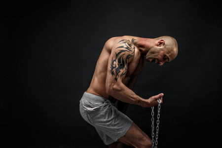 Portrait of muscular tattooed sportsman tearing metal chain.Black backgroundの写真素材