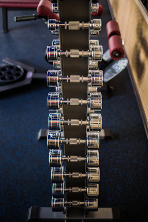 Sport Background. Rack of dumbbells in health club. Shelf with metal on gym studio room backdrop.の写真素材