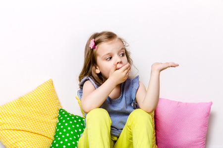 Portrait of kid showing surprise with hand covering mouth.Colorful pillowsの写真素材