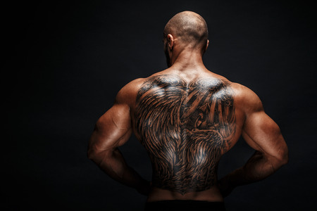 Unrecognizable muscular man with tattoo on back against of black background. Isolated.の写真素材