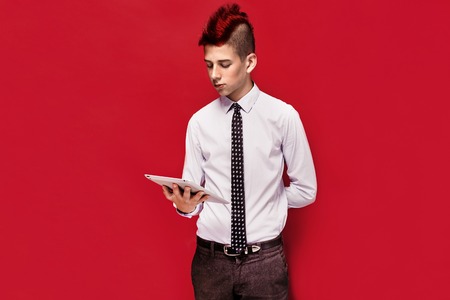 Portrait of red-haired teen punk with tablet against of red background. Isolated.の写真素材