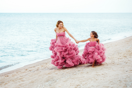 Mother and little daughter in pink dress on the beachの写真素材