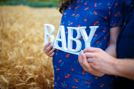 Close-up of unrecognizable husband hugging his wife's pregnant belly on straw fieldの写真素材