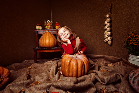 portrait of adorable smiling girl posing with orange pumpkin in roomの写真素材