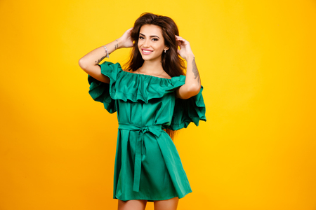 Studio portrait of beautiful brunette woman in elegant green dress smiling at camera on yellow backgroundの写真素材