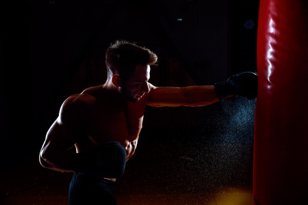 Young male boxer hitting punching bag on black background.の写真素材