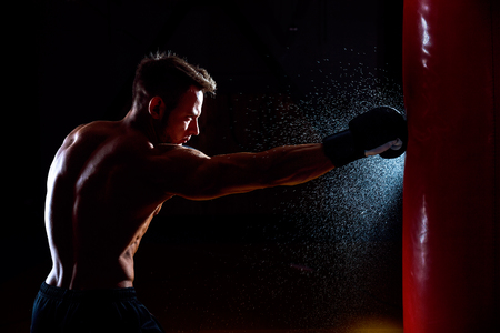Young male boxer hitting punching bag on black background.の写真素材