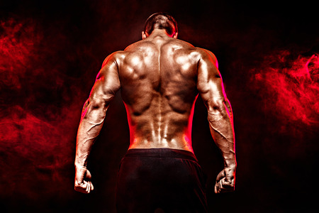 The back view of torso of attractive male body builder on dark smoky background.の写真素材