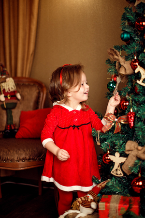 Standing girl puts decorations to a Christmas tree. Vertical indoors shot.の写真素材